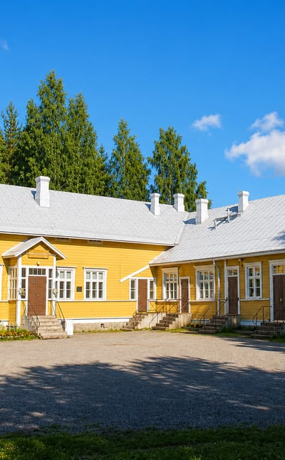 Yellow timber building with a metal roof beside spruce woods in Utra, Joensuu.