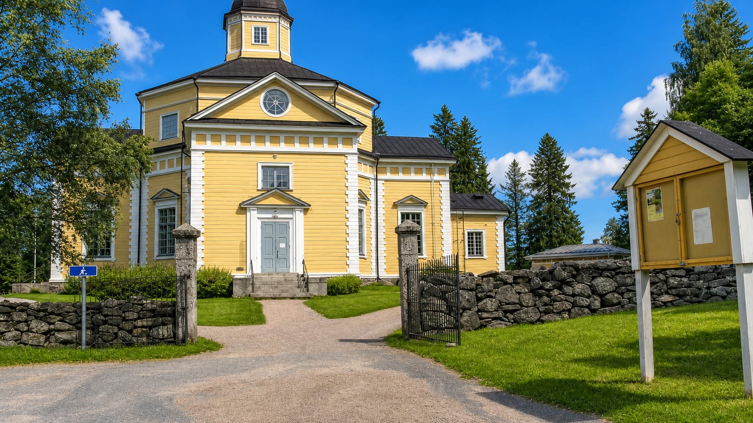 Juuka's yellow neoclassical wooden church with a clock and domed cupola behind a stone wall and gravel path.