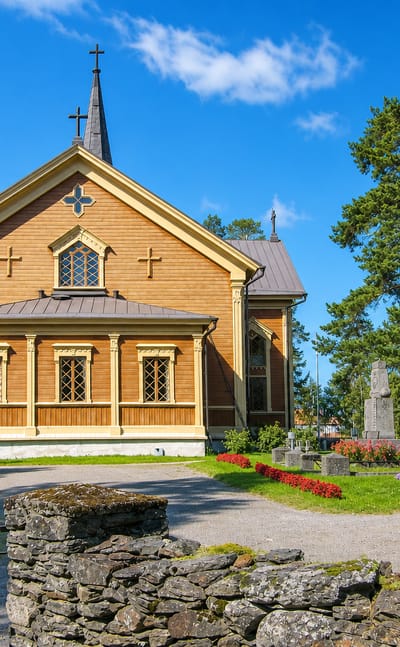 Yellow wooden church with a dark spire beside its cemetery in Kontiolahti, Finland.