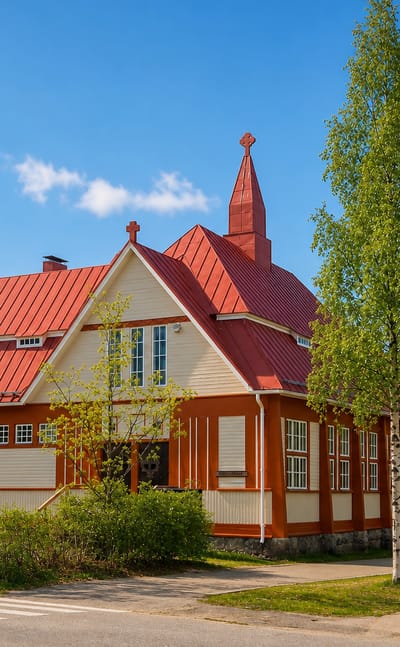 Wooden church with a red roof and cross-topped spire on a birch-lined street in Nurmes, Finland.