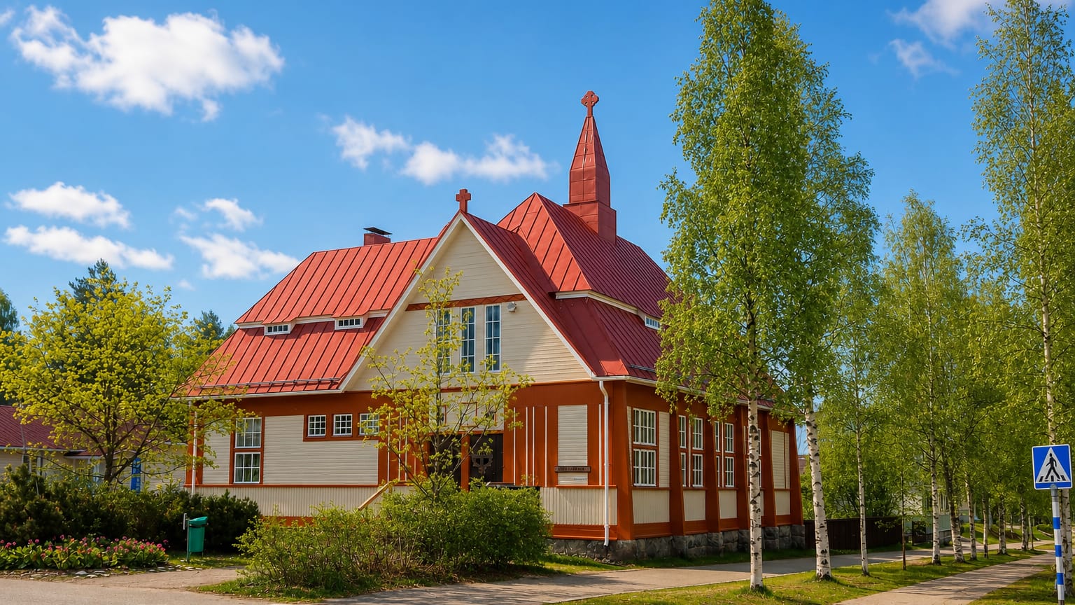 Wooden church with a red roof and cross-topped spire on a birch-lined street in Nurmes, Finland.