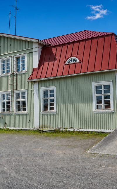 Historic green wooden Haapajarvi railway station with a red hipped roof and station nameboard under a blue sky.