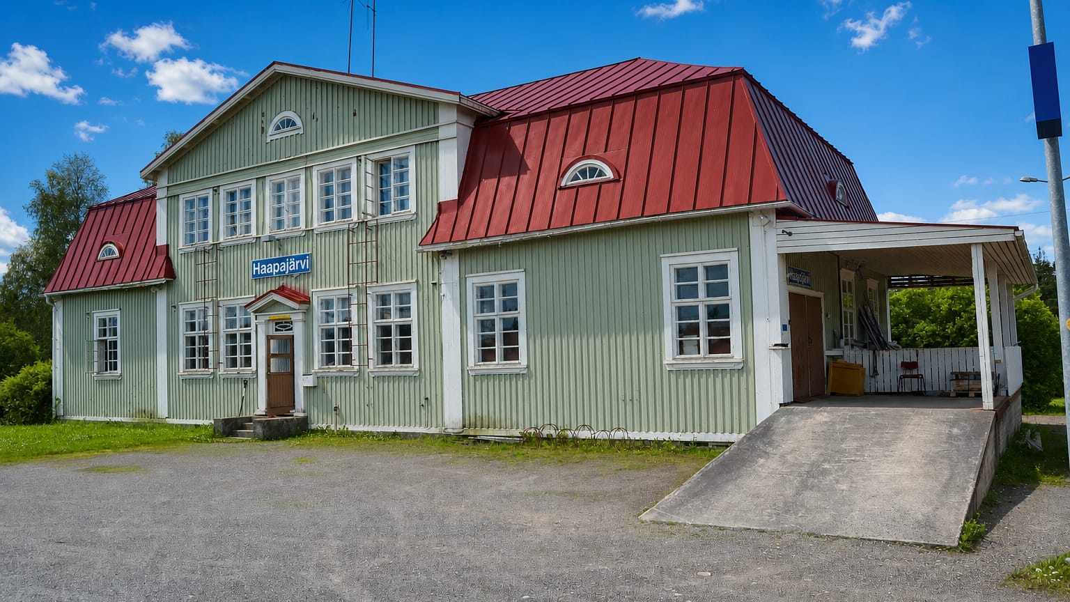 Historic green wooden Haapajarvi railway station with a red hipped roof and station nameboard under a blue sky.