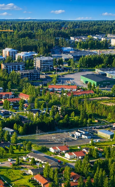 Aerial daytime view of Kempele, Finland, with apartment blocks, red-roofed houses and forest under a blue sky.