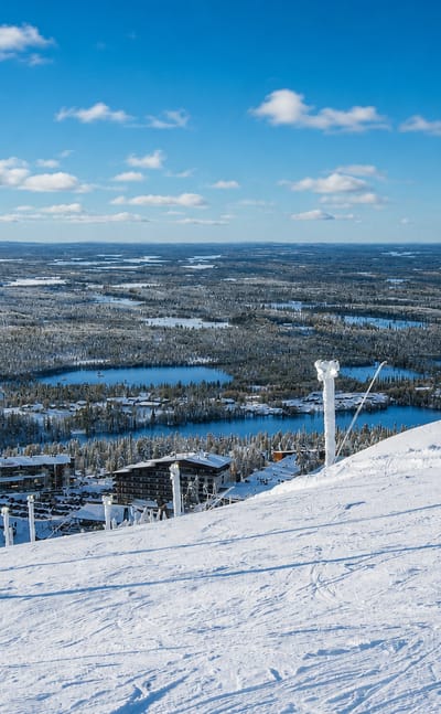Winter view from Ruka fell over the Kuusamo resort, a snow-laden slope, frosted poles and frozen lakes below.