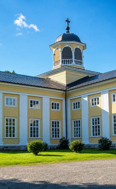 Yellow-and-white neoclassical wooden church with a cupola bell tower under a summer sky in Liminka, Finland.