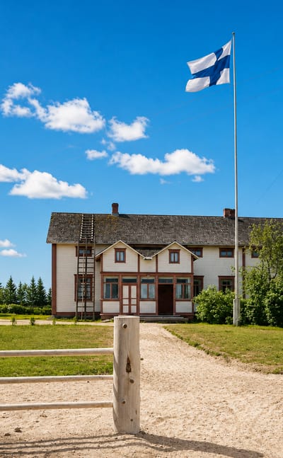 Traditional cream farmhouse, red wooden barns, a Finnish flag and a bicycle at a rural homestead in Nivala, Finland.