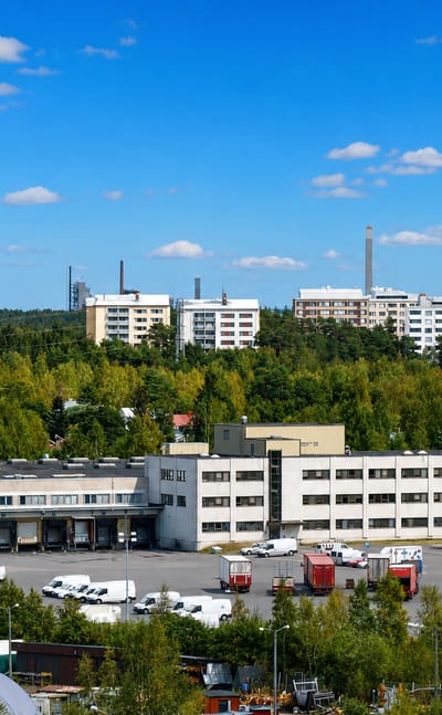 Daytime view over Alppila, Oulu, with a water tower, white apartment blocks and an industrial estate amid forest.