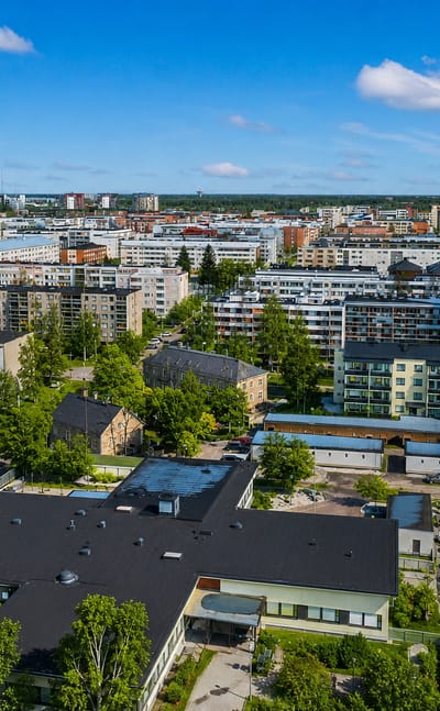 Aerial daytime view of the Hollihaka district in Oulu, Finland, with mid-rise apartment blocks, parking lots and leafy trees.