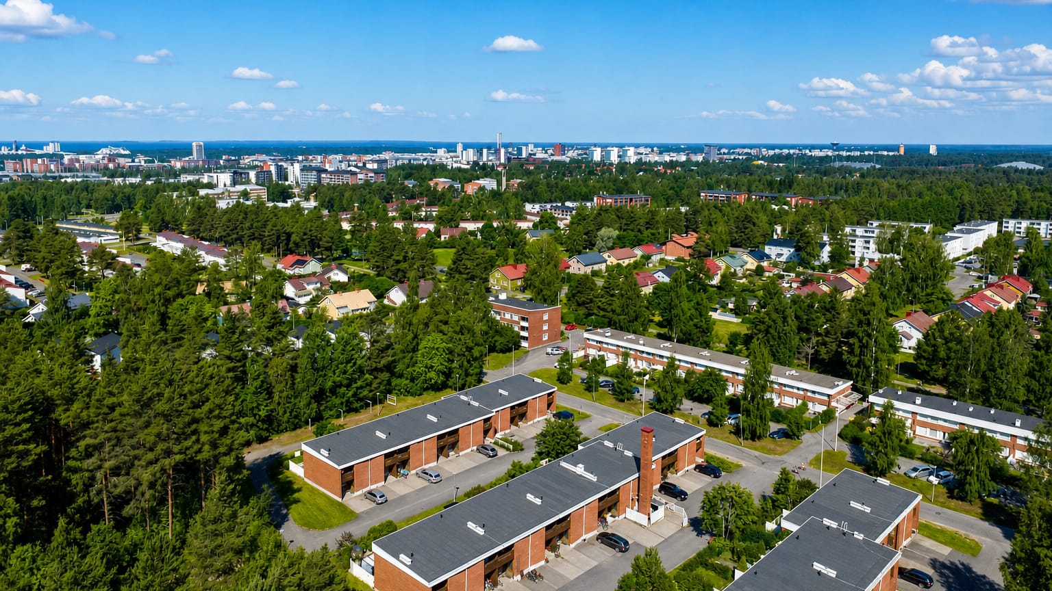 Aerial view of red-brick terraced housing and pine woods in Höyhtyä, with the Oulu skyline beyond.