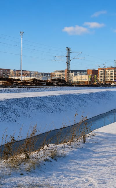 Snow-covered railway yard beside red-brick apartment blocks under a clear blue winter sky in Karjasilta, Oulu, Finland.