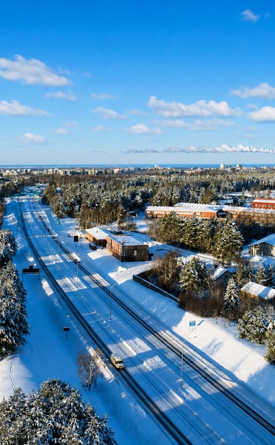 Snow-covered motorway through pine forest at Kynsilehto, Oulu, with the city's industrial skyline beyond.