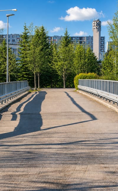 Pedestrian footbridge leading toward apartment blocks and towers in Myllytulli, Oulu, on a sunny summer day