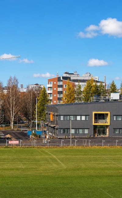 Sports field before an office building and construction cranes among autumn birches in Nuottasaari, Oulu.