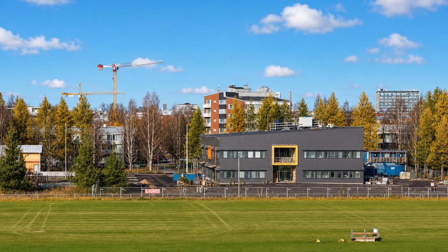 Sports field before an office building and construction cranes among autumn birches in Nuottasaari, Oulu.