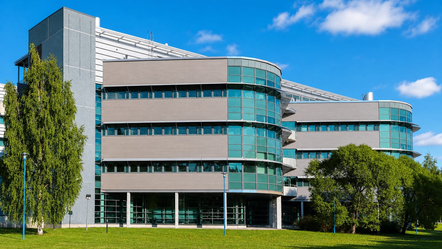 Modern green-glass office building set among lawns and birches at Peltola in Oulu.