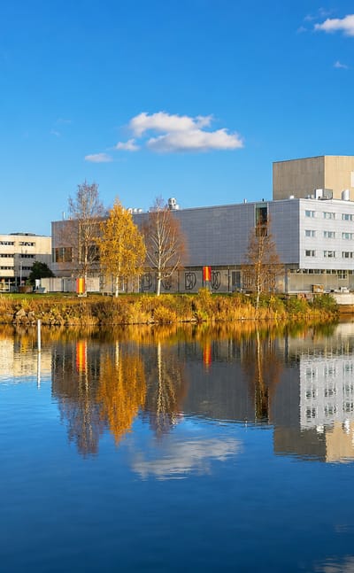 Pokkinen waterfront in Oulu, Finland, modern white buildings and autumn trees mirrored in calm river water under a blue sky