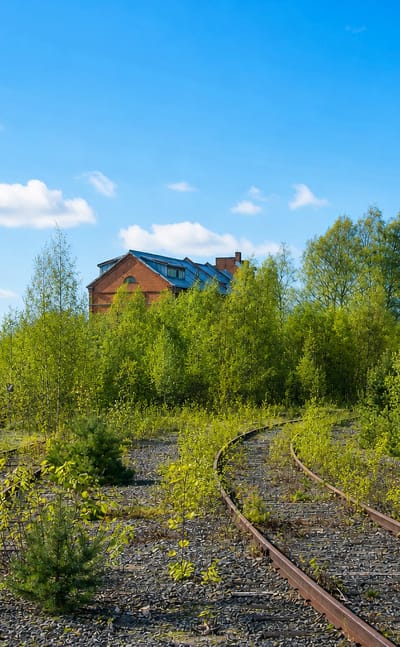 Disused railway tracks curving through green birch saplings past brick buildings and a silo in Toppila, Oulu, Finland