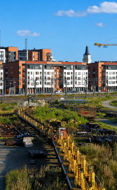 Modern red-brick and white apartment blocks of Vanhatulli, Oulu, rising beyond former railway yards under a clear blue sky.