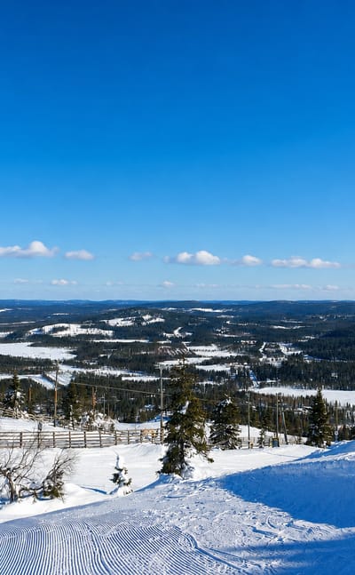 Snowy ski slope and lift atop Iso-Syöte fell in Pudasjärvi, Finland, overlooking forested hills and frozen lakes
