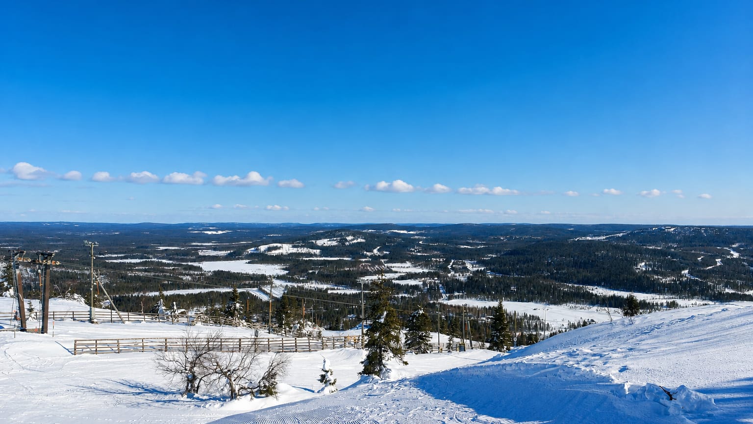 Snowy ski slope and lift atop Iso-Syöte fell in Pudasjärvi, Finland, overlooking forested hills and frozen lakes