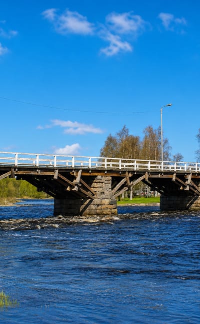 Wooden bridge on stone piers spanning the rapids of the Pyhäjoki river under a blue summer sky, Pyhäjoki, Finland