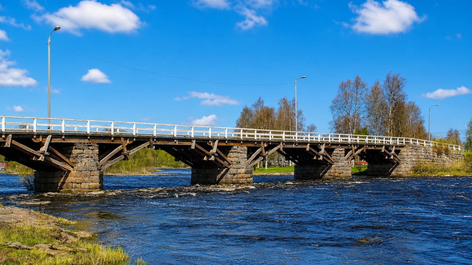 Wooden bridge on stone piers spanning the rapids of the Pyhäjoki river under a blue summer sky, Pyhäjoki, Finland