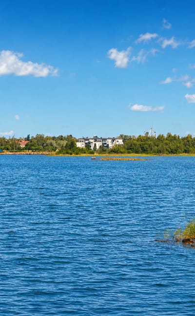 Raahe's low skyline across the blue Gulf of Bothnia, a church spire at left and a tall waterfront building at right under a summer sky.