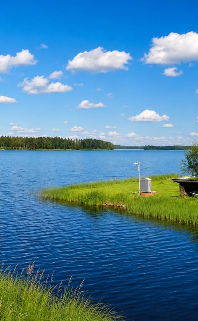 Calm lake with a grassy point and small red boathouse near Reisjärvi, Finland.