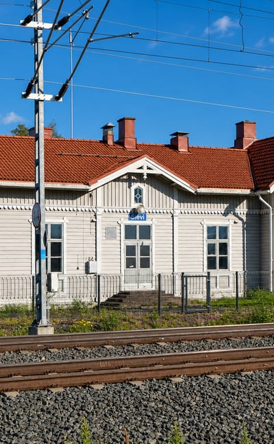 Grey wooden railway station with a red-tiled roof beside the tracks in Sievi, Finland.