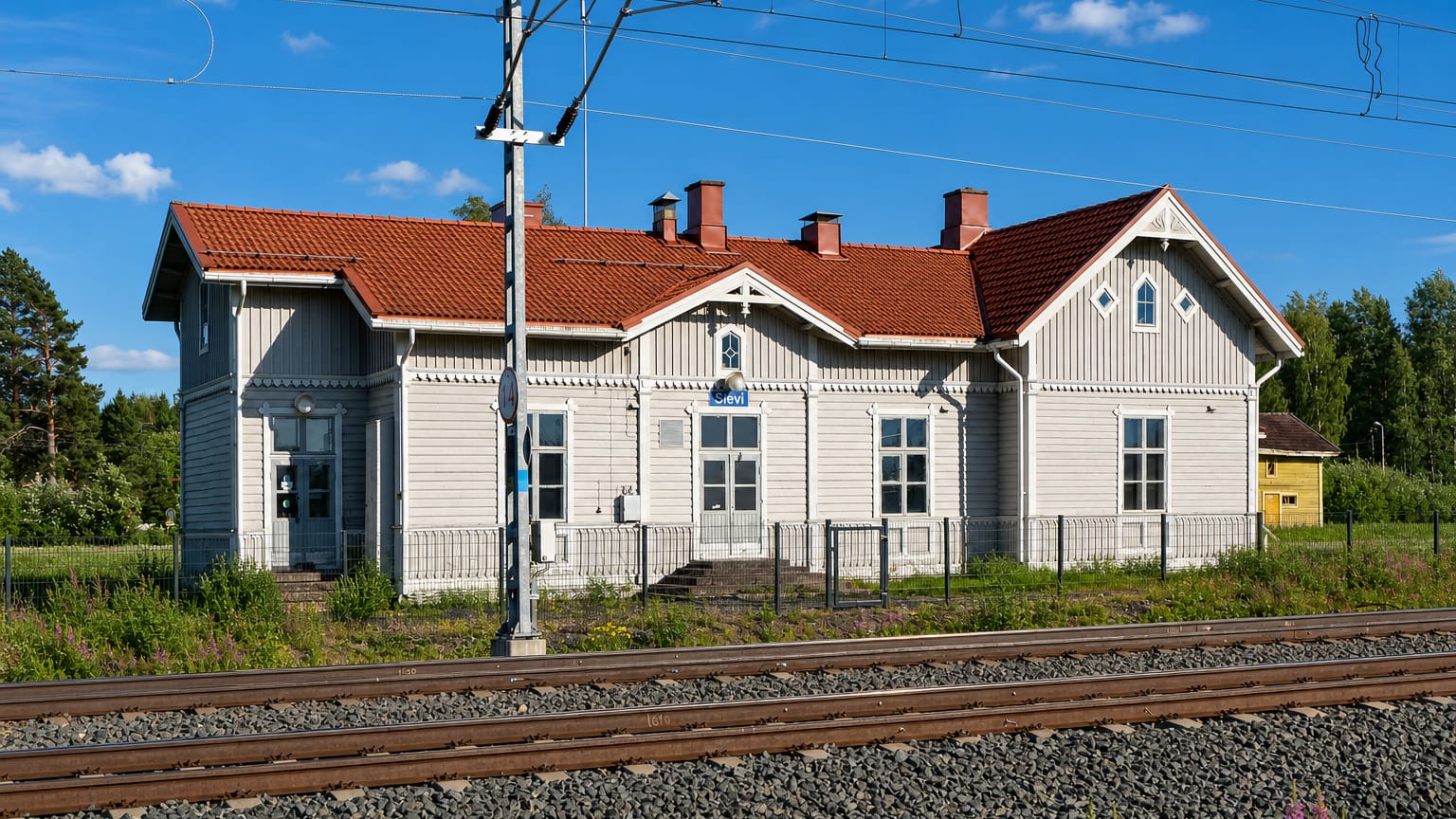 Grey wooden railway station with a red-tiled roof beside the tracks in Sievi, Finland.
