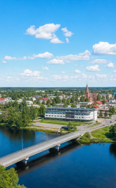 Aerial view of Taivalkoski by its lake and bridge, with a red-brick church and low buildings ringed by forest.