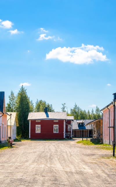 Historic pink dairy-museum buildings marked KIRJASTO and 1919 along a gravel yard in Tyrnava