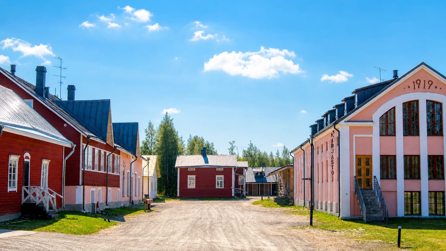 Historic pink dairy-museum buildings marked KIRJASTO and 1919 along a gravel yard in Tyrnava