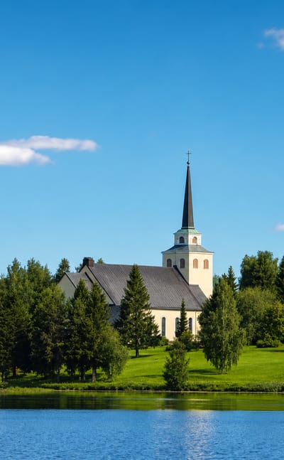 Kiuruvesi's yellow lakeside church and tall spire above a green wooded shore reflected in the calm summer lake