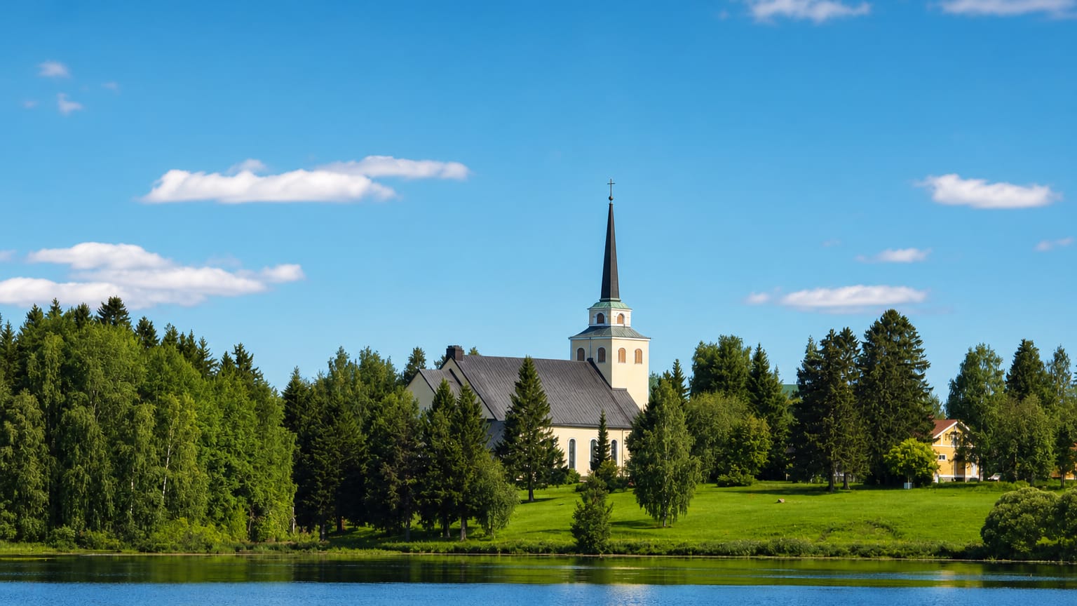 Kiuruvesi's yellow lakeside church and tall spire above a green wooded shore reflected in the calm summer lake