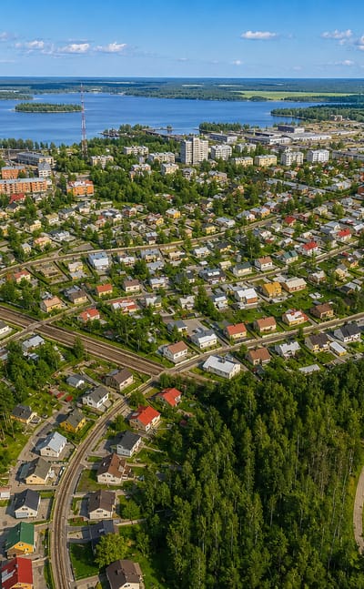 Aerial view of wooden houses and rail lines in Niirala, Kuopio, with Lake Kallavesi stretching beyond.