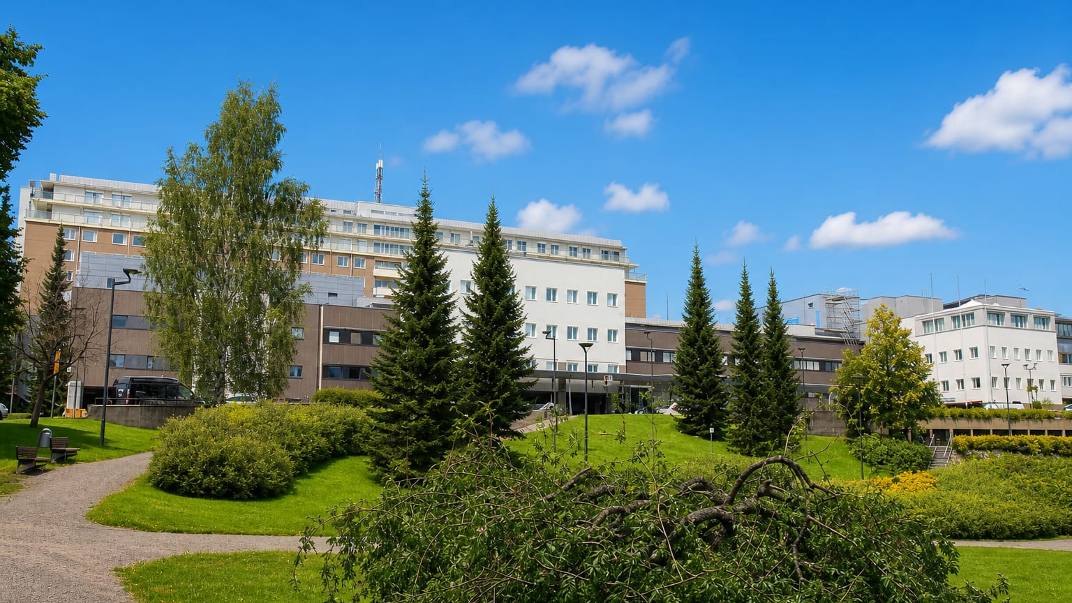 Large white hospital-style complex above a park with spruces and birches in Puijonlaakso, Kuopio.