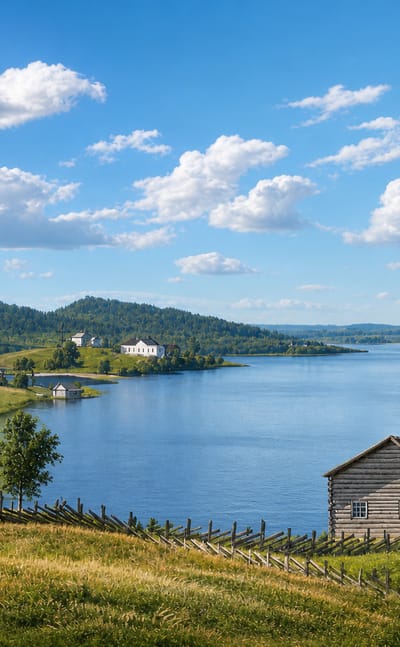 Rautalampi, Finland: a traditional log cabin and rail fences on green hills above a broad blue lake under summer clouds.