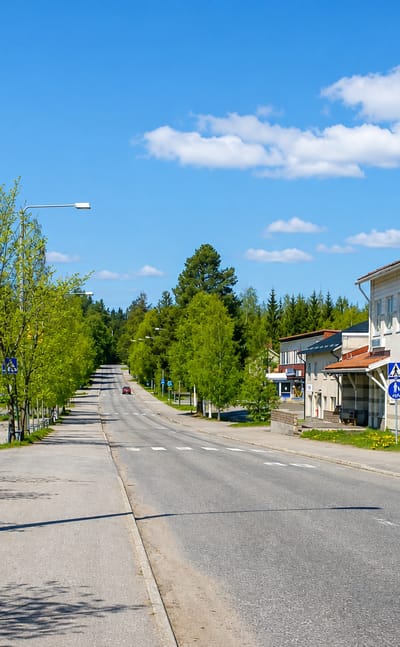 Quiet tree-lined main street through Rautavaara, Finland with a modern building and road signs.