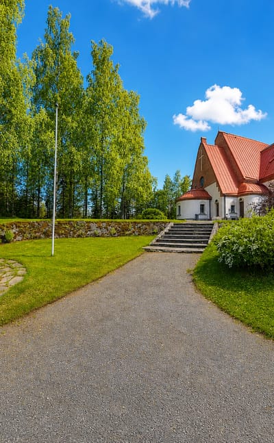 Siilinjärvi's red-brick church with a tall spire and tiled roof beside a war memorial in a green churchyard.