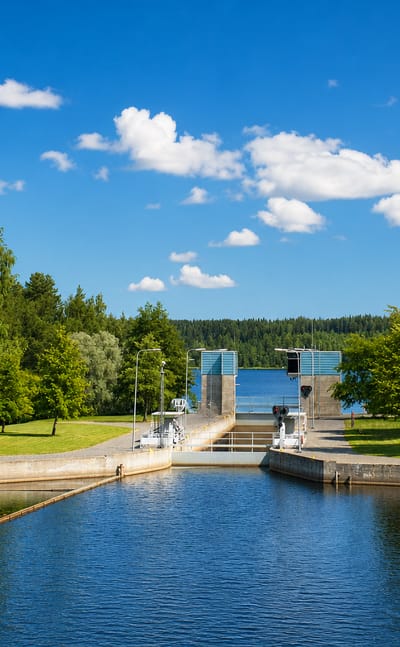 A canal lock and calm waterway framed by lush green birches under a blue summer sky in Tervo, Finland.