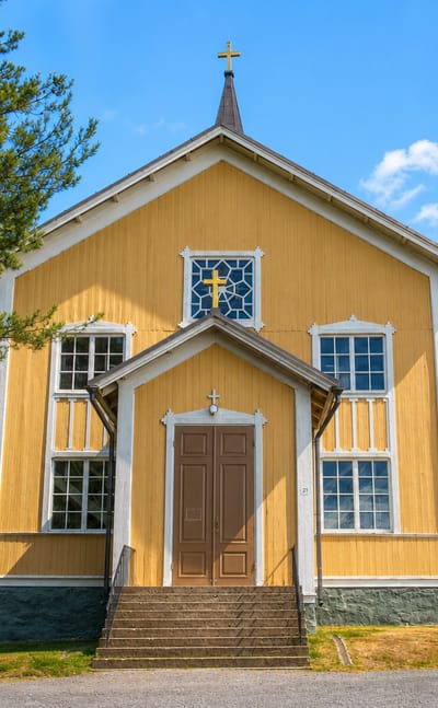 Yellow wooden church with a cross-topped spire in Tuusniemi under a clear blue sky.