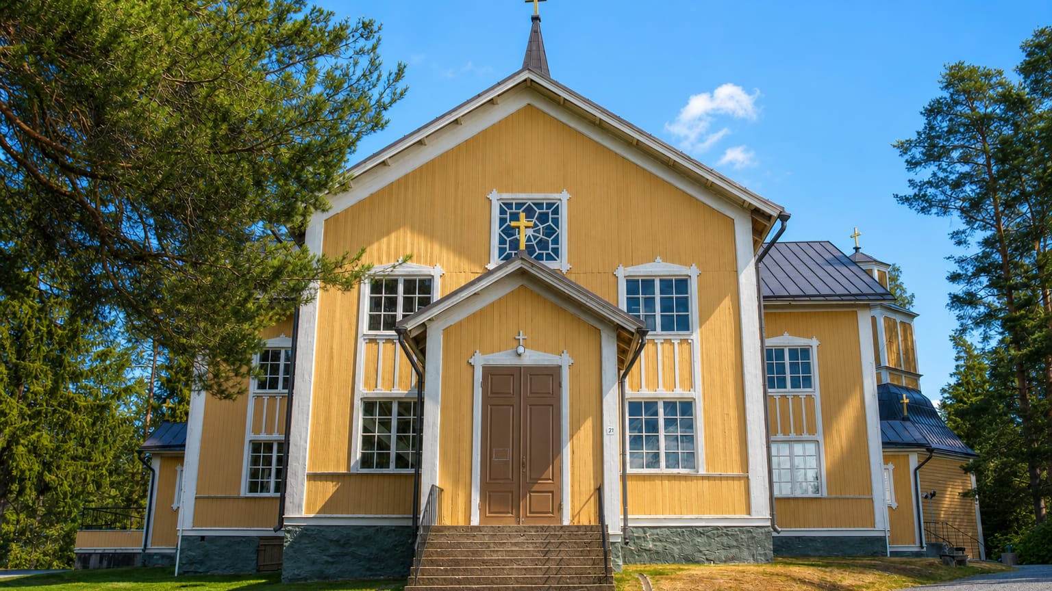 Yellow wooden church with a cross-topped spire in Tuusniemi under a clear blue sky.