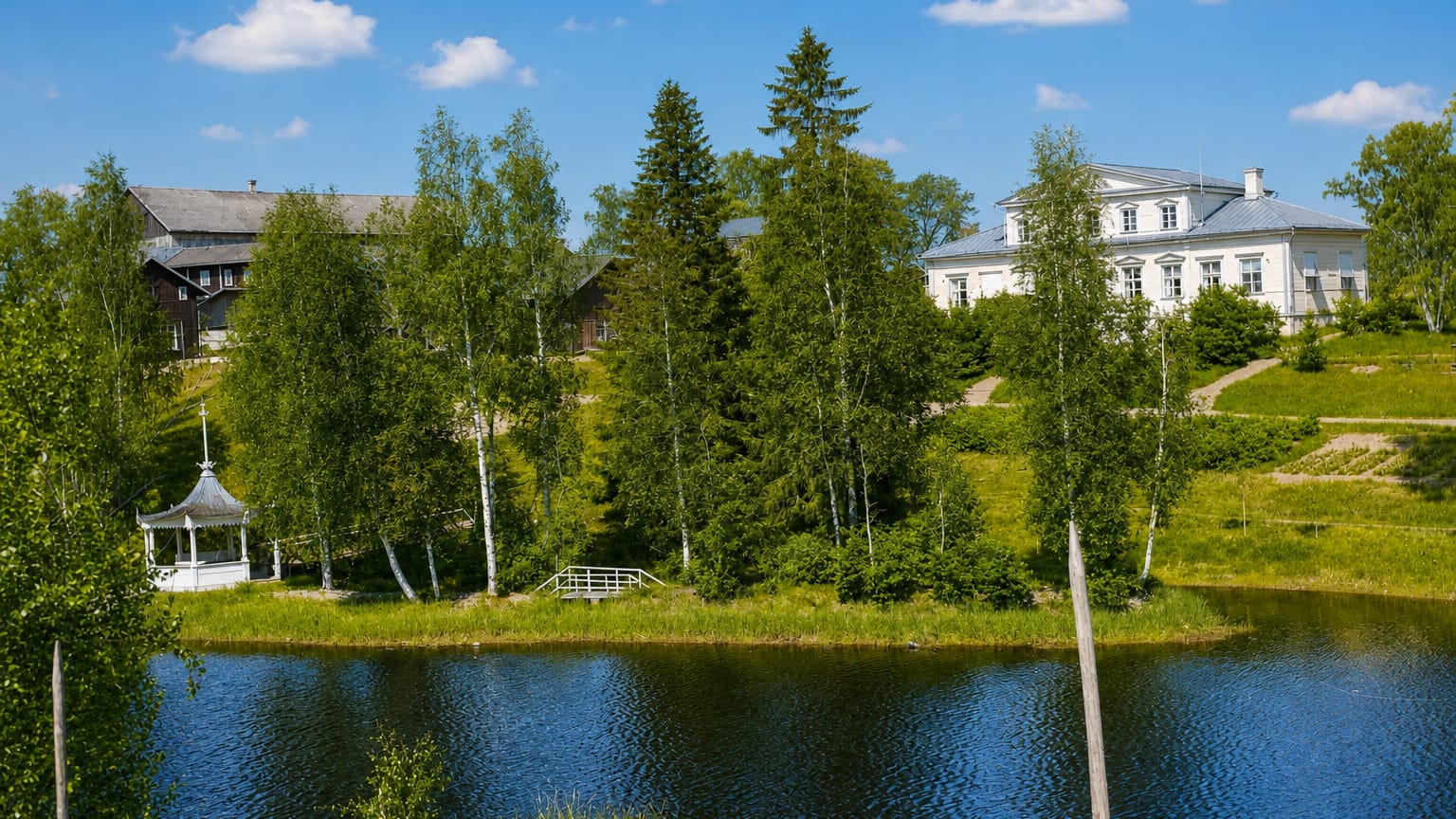 Summer lakeside in Vieremä, Finland, with white wooden buildings, a gazebo and footbridge among birch and spruce trees.
