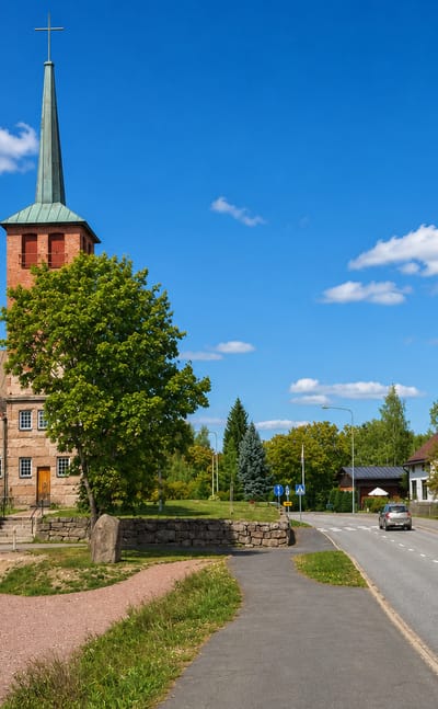 Eura, Finland's granite church with a green copper spire beside a quiet village street on a sunny day.
