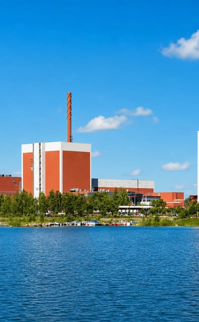 Olkiluoto Nuclear Power Plant at Eurajoki, Finland, its red reactor buildings and striped stacks beside calm blue coastal water