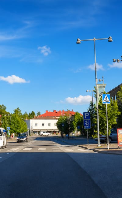 Kankaanpaa town centre with the Keskustori commercial building, crossing and parked cars under a blue summer sky.