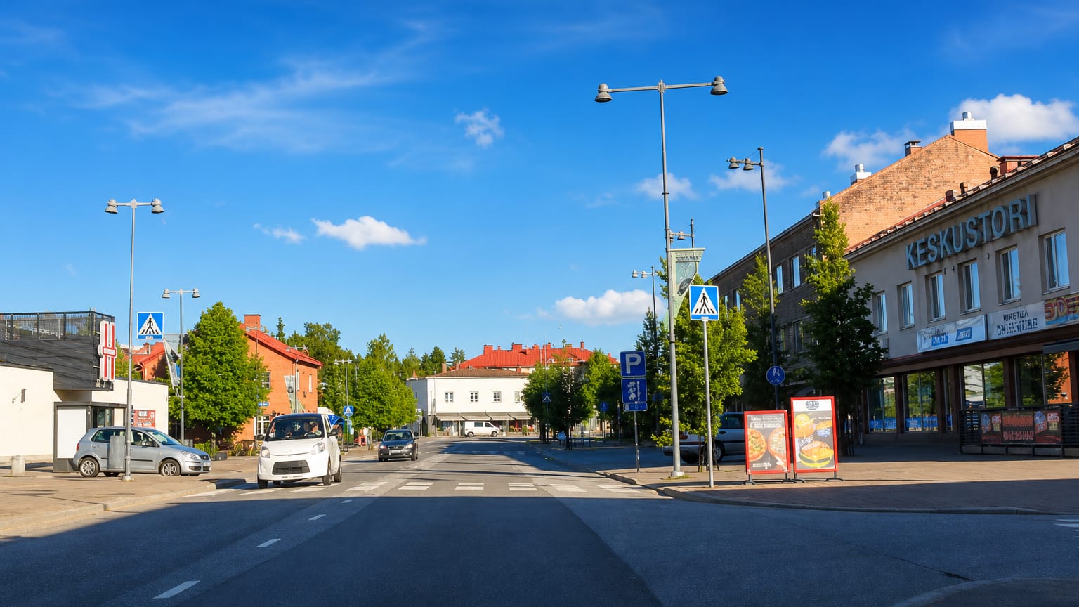Kankaanpaa town centre with the Keskustori commercial building, crossing and parked cars under a blue summer sky.