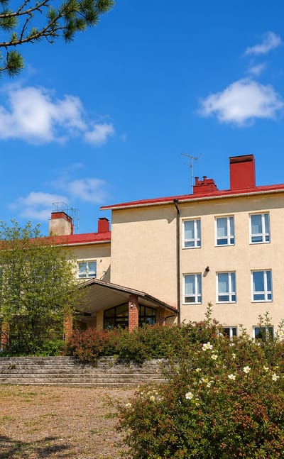 Beige school building with a red roof and entrance steps in Kiukainen, Finland